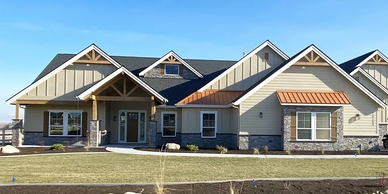 Front view of a house with light brown siding, natural wood eves, stone, and dark brown shutters.