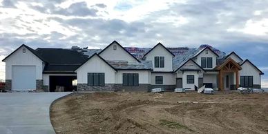 Front view of large home with white siding brown and grey stonework RV bay and natural wood entry.