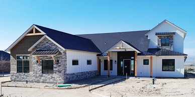 Custom home with white siding, natural wood beams, and grey exterior stonework.