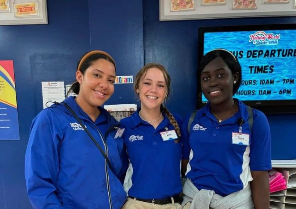 Three smiling employees in blue uniforms at a customer service desk.