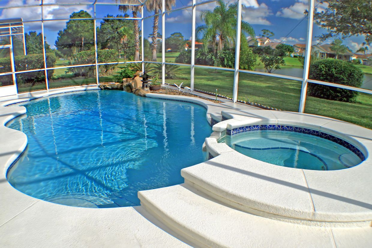 A clear blue swimming pool and hot tub in a screened patio with lush greenery outside.
