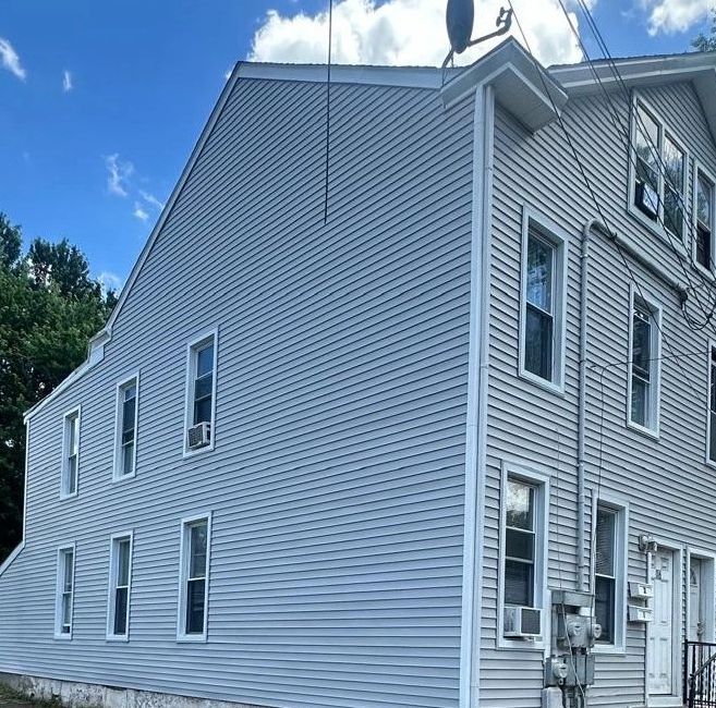 Exterior of a gray multi-story house with multiple windows and air conditioning units.