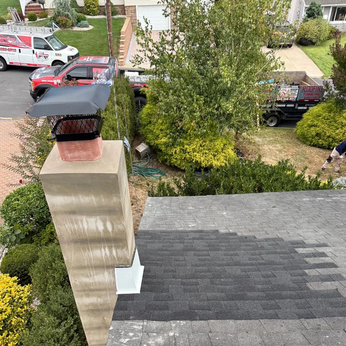 A newly roofed chimney with roofing company trucks in the background.
