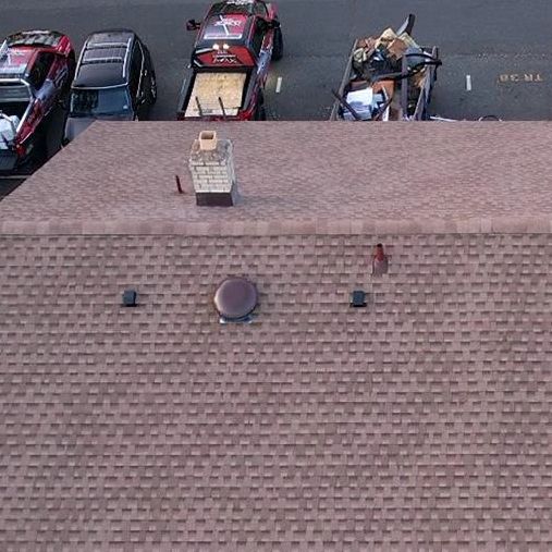 Aerial view of a brown shingle roof with vehicles parked at the edge.