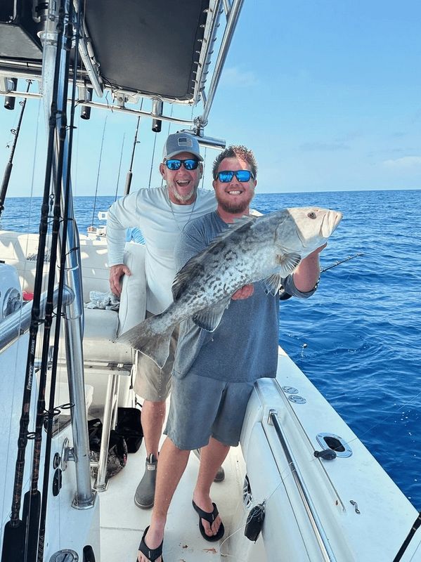 Two men on a boat proudly holding a large fish they caught during a fishing trip.