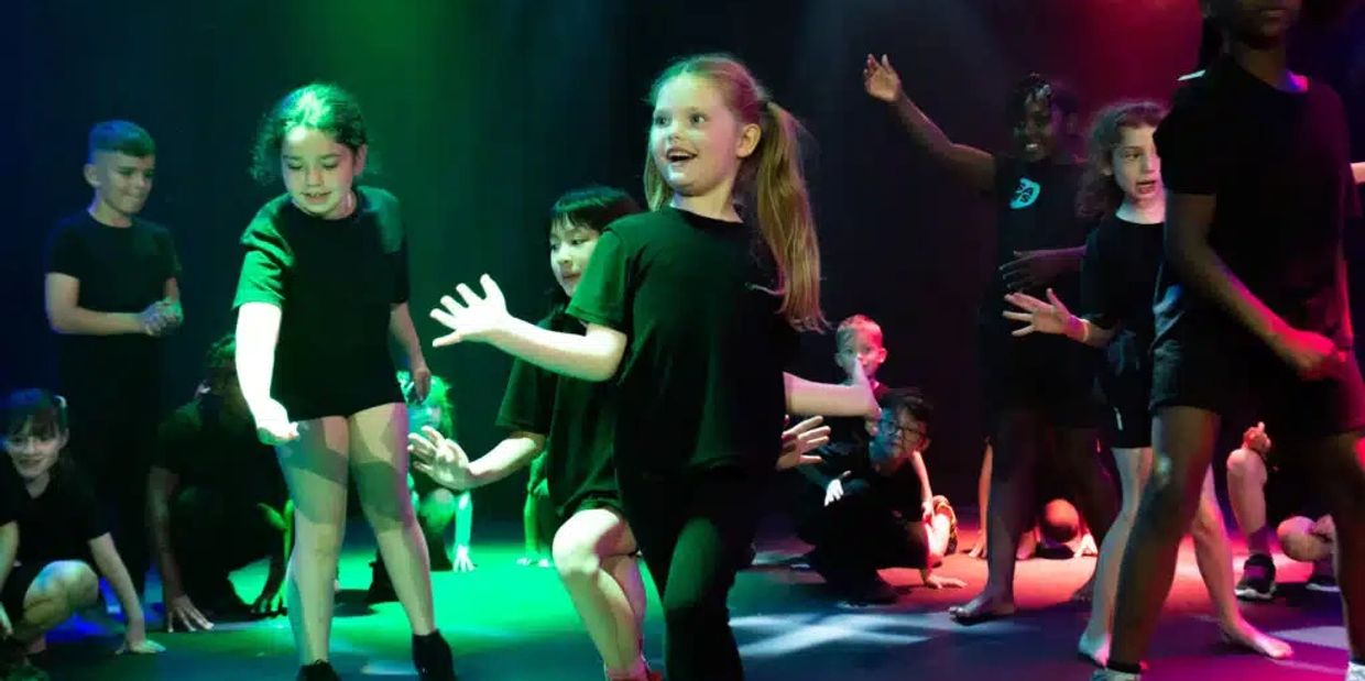 Children performing a lively dance on stage with colorful lighting.