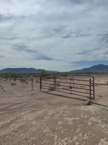 A metal gate in a desert landscape with mountains and cloudy sky.