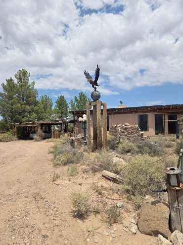 Eagle statue on wooden poles near a rustic house in a desert setting.