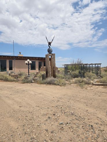 Desert landscape with a statue and building under a cloudy sky.