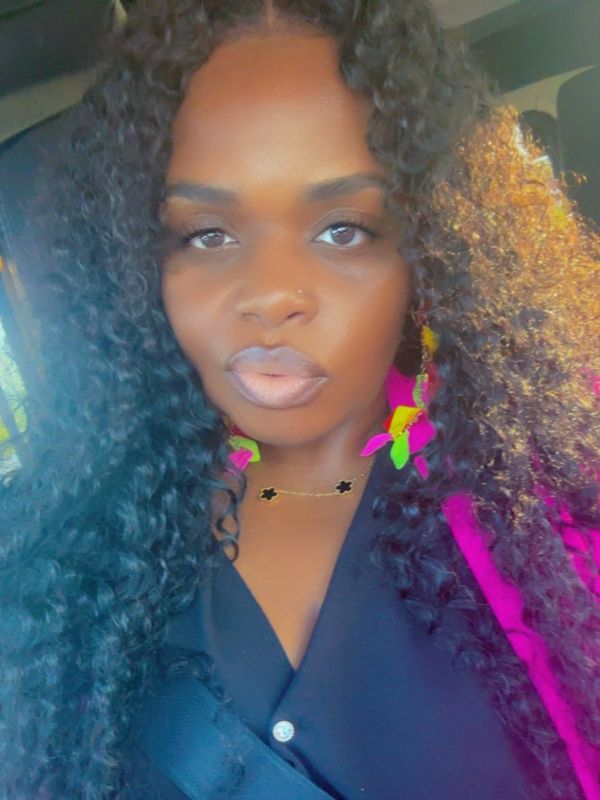 Woman with curly hair wearing a black top and pink jacket.