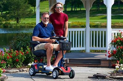 A man on a mobility scooter with a woman standing behind him in a garden.