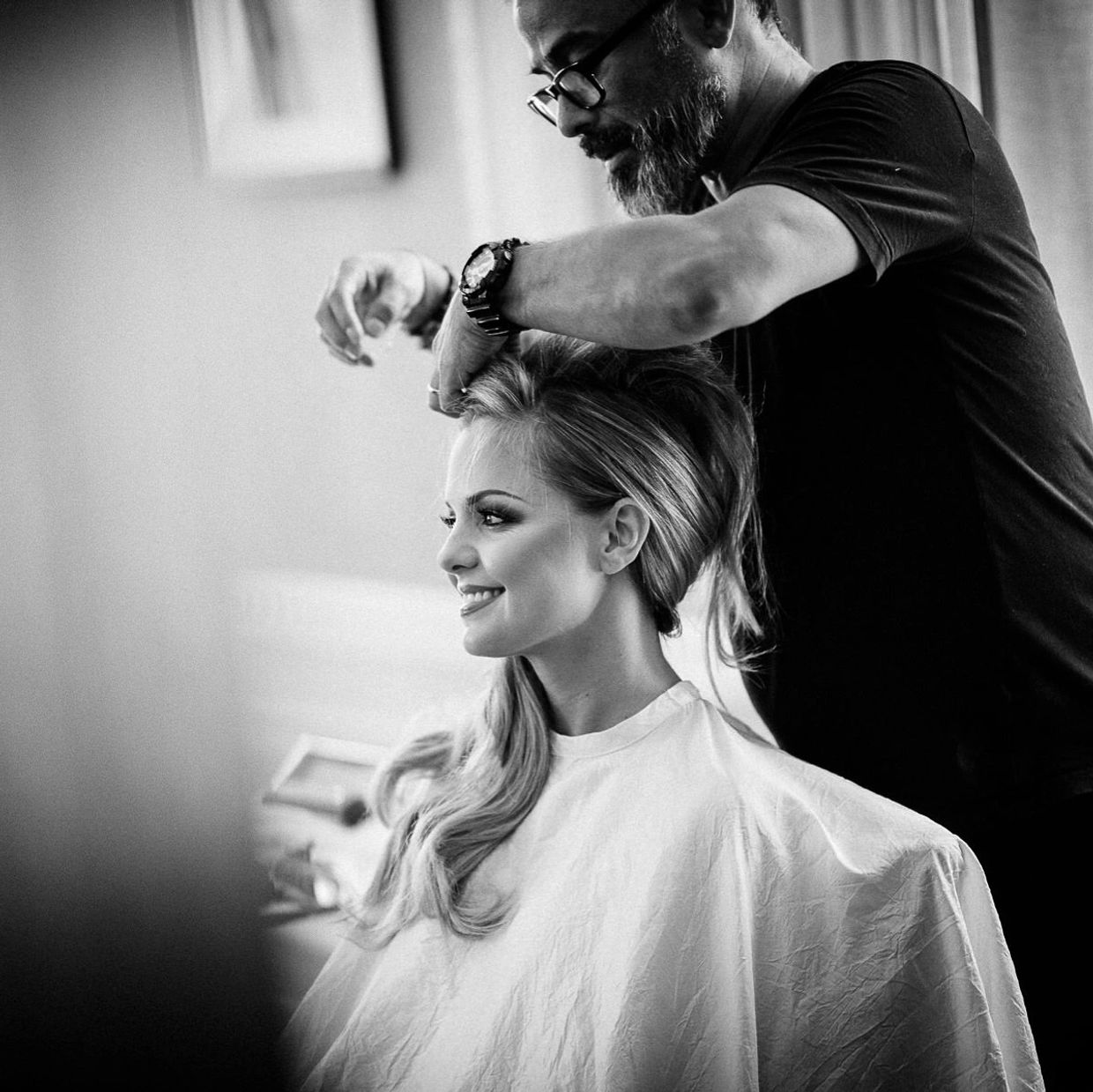 Hairdresser styling woman's hair with a smile.