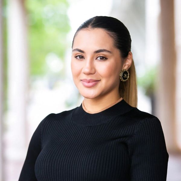 Confident woman smiling with hair tied back and wearing black top.