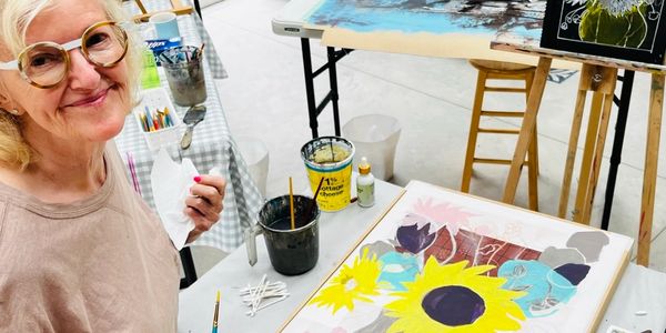 Woman painting a sunflower artwork at a table.
