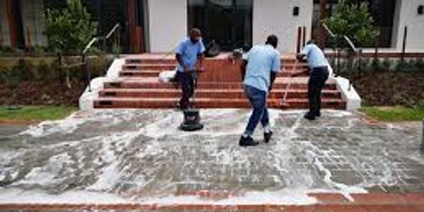 Three people cleaning a large outdoor tiled area with soap and brushes.