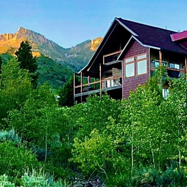 A cozy cabin nestled among green trees in a mountainous landscape during sunset.
