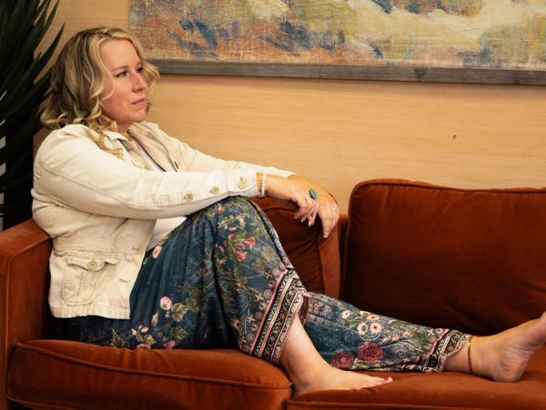 Woman relaxing on an orange couch wearing floral pants and a white jacket.