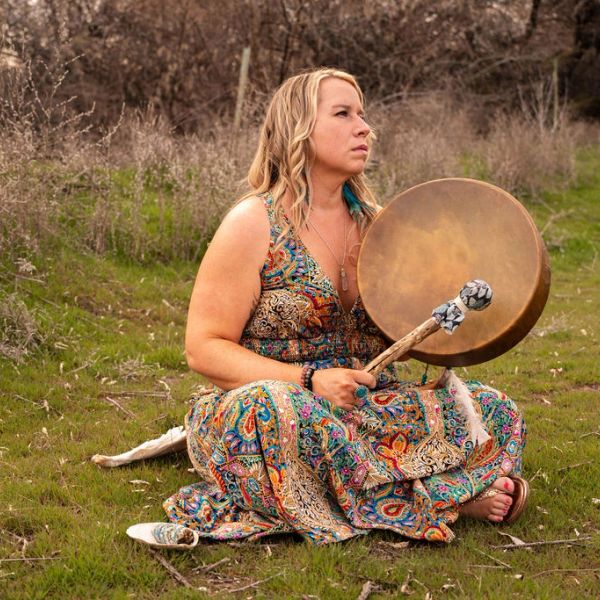 Woman in colorful dress playing a drum outdoors.