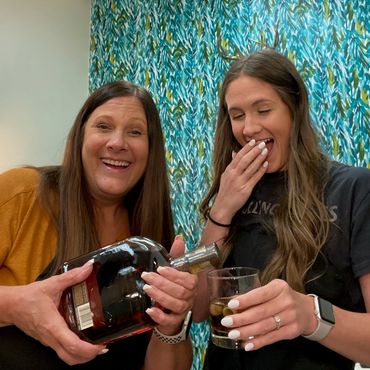 Two women smiling as one pours a drink into a glass.