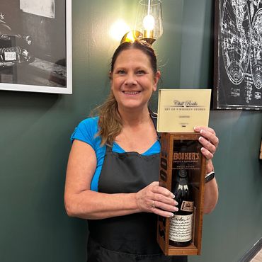 Smiling woman holding a boxed bottle of Booker’s bourbon whiskey.