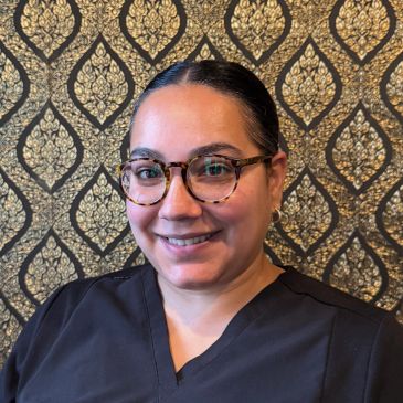 A smiling woman with glasses in front of a patterned gold and black background.