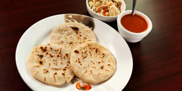 Plate of 3 pupusas served with sauce and a side.