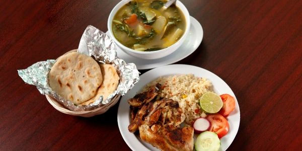 An overflowing plate of food, a bowl of soup, and a basket of pupusas.