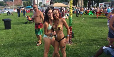 Two women in bikinis posing happily at an outdoor event on a sunny day.