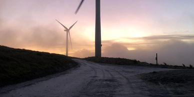 Wind turbines against a sunset sky on a dirt road.