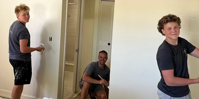 Three people painting a white wall in a room.