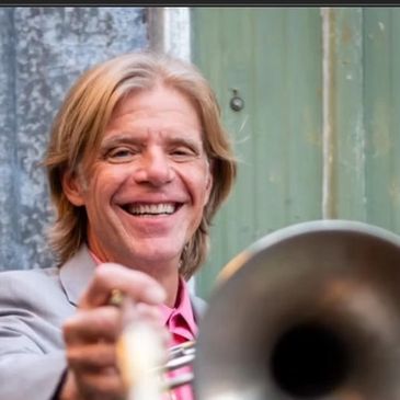Man smiling while playing trumpet outdoors.