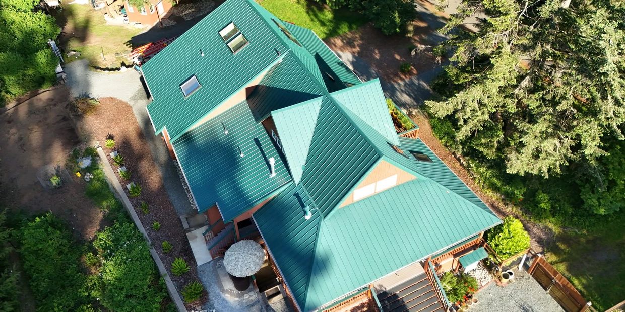 Aerial view of a large house with a green metal roof surrounded by trees and garden.
