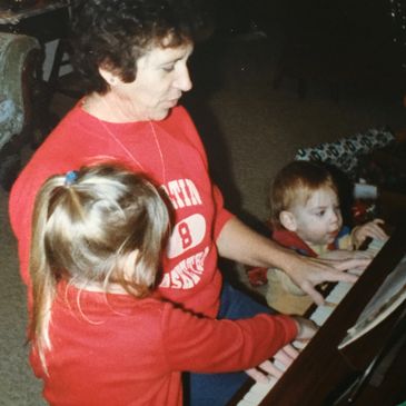 Adult and two children playing piano together.