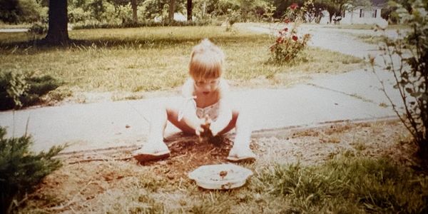Little girl playing with soil outside near a road.