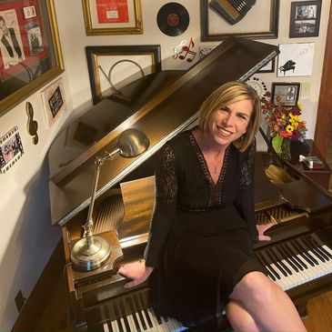Woman sitting on a grand piano smiling.