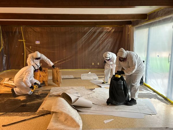 Four workers in protective suits removing flooring in a room under renovation.