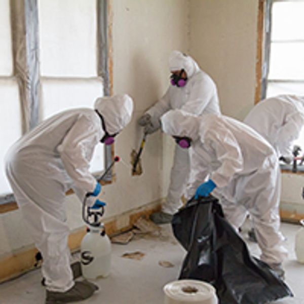 People in protective suits removing hazardous materials indoors.