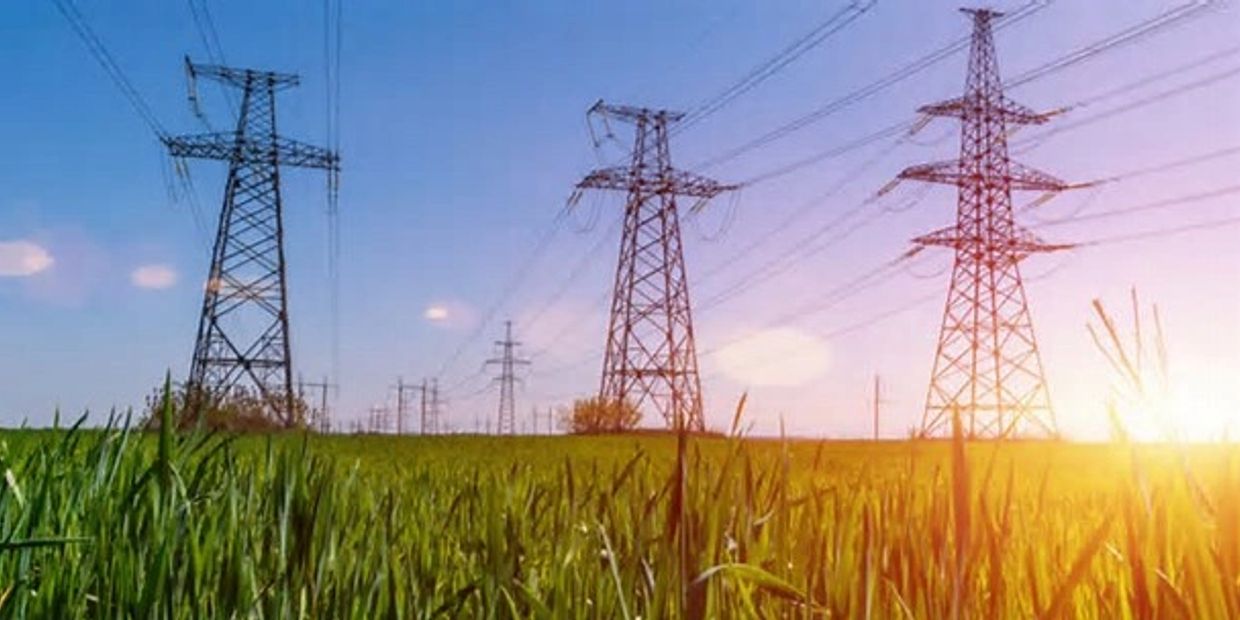 Electric power lines stretch across a green field at sunset.