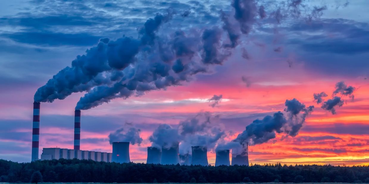 Industrial smokestacks emit smoke against a vibrant sunset sky.