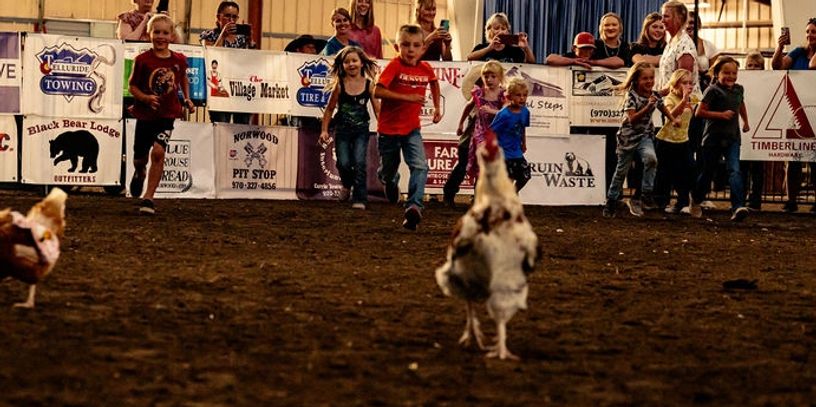 Children excitedly chase chickens in a lively barnyard race event.