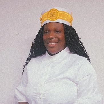Smiling woman in white attire and yellow hat.