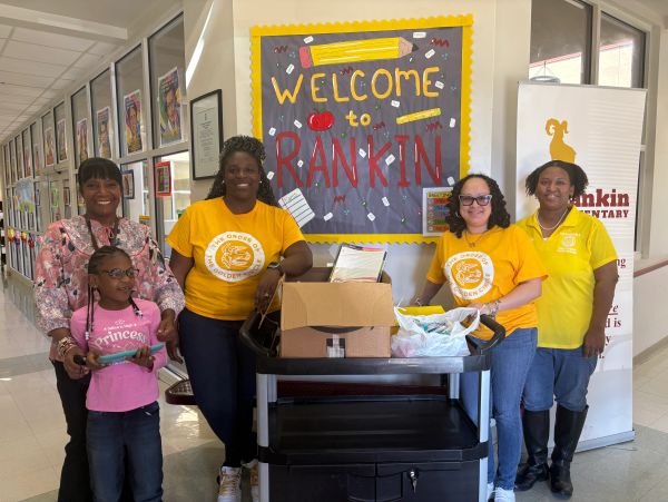 Group of smiling adults and a child in a school hallway with a welcome sign.