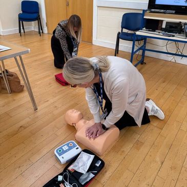 Woman practicing CPR on a training mannequin in a classroom setting.