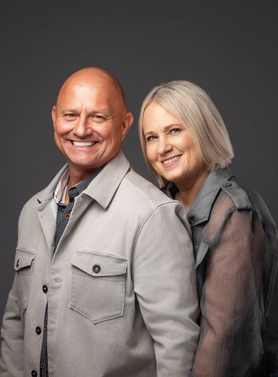Smiling middle-aged couple posing together against a dark background.