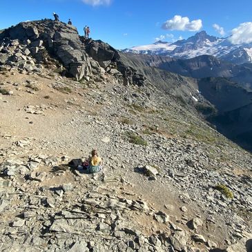 Hikers resting on a rocky mountain slope with snowy peaks in the background.