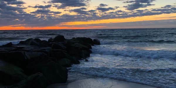 Sunset over ocean waves with rocks and a cloudy sky.