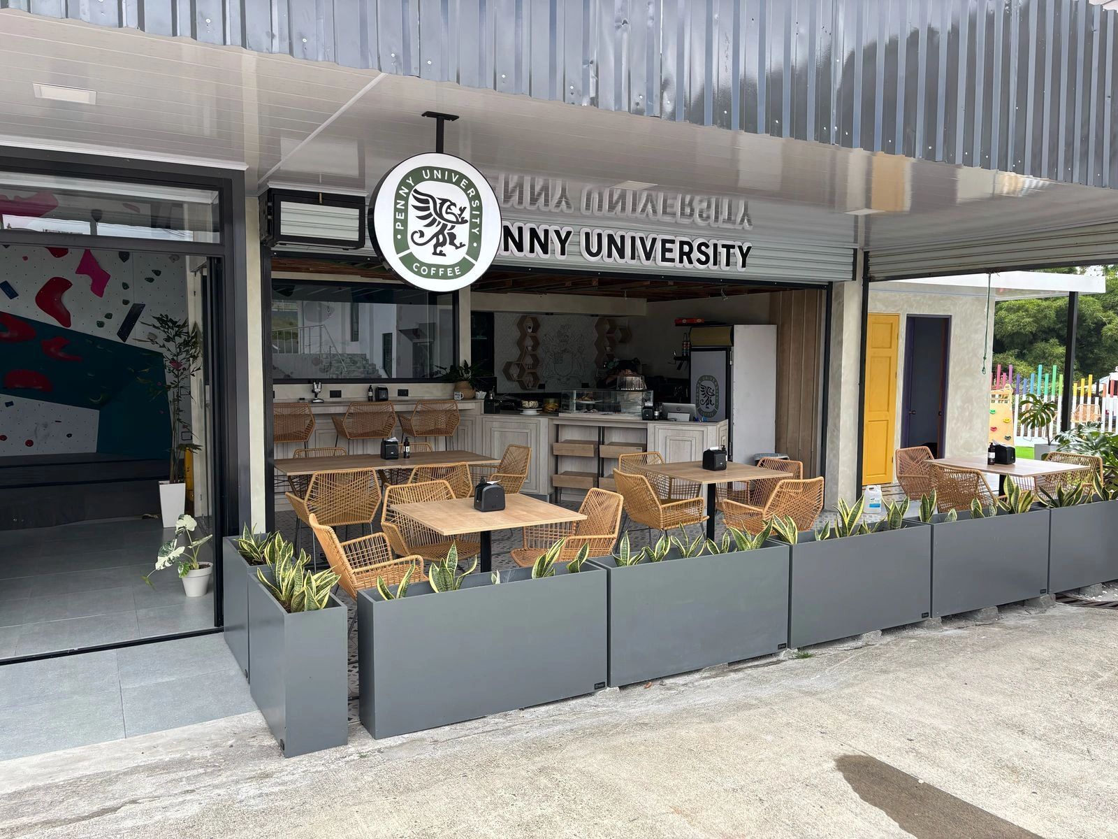 Fachada de cafetería con mesas y sillas de mimbre.