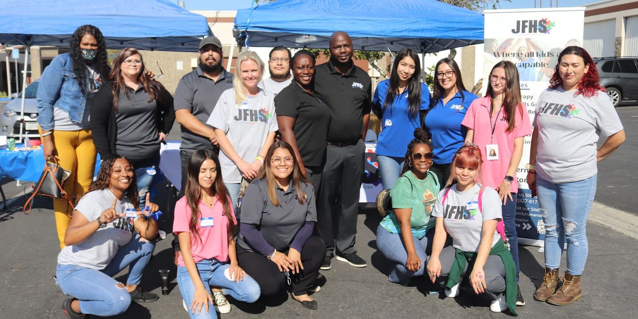 Group photo of diverse staff at an outdoor event under blue tents.
