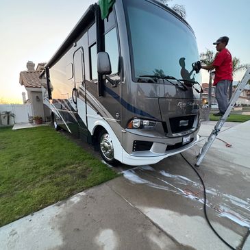 Man cleaning the windshield of a large RV with a ladder beside him.