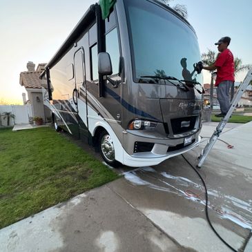 Man cleaning the windshield of a large RV with a ladder beside him.
